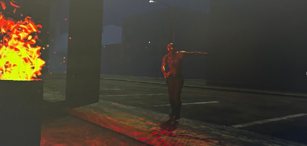 In-game scene: survivor in a dark urban environment illuminated by fire